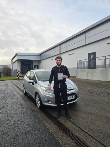 Man holding documents next to a silver car outside a building.